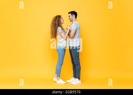 In voller Länge Porträt von jungen glücklichen interracial Paar stehen nah in die Augen schauen und halten sich die Hände in isolierten gelben Studio Rücken Stockfoto