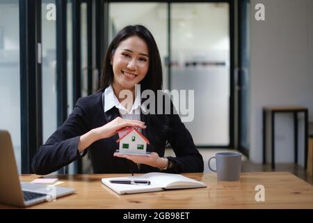 Ein Immobilienmakler demonstriert das Haus-Modell für Kunden, die sich für den Kauf einer Hausversicherung interessieren. Das Konzept der Hausversicherung und Immobilien Stockfoto