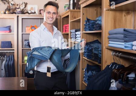 Fröhlicher Mann, der sich für eine neue Hose entscheidet Stockfoto