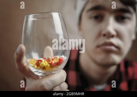 Trauriger Kerl mit einem Glas Pillen und Drogen. Behandlung und Prävention in Quarantäne. Kranker Mann. Stockfoto