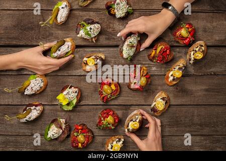 Hände nehmen Bruschettas mit verschiedenen Belägen auf Holzoberfläche Stockfoto