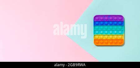 POPIT auf blauem und pinkem Hintergrund mit Kopierbereich. Beliebte Silikon bunte Antistress Pop it Spielzeug für Kind. Draufsicht von oben. Einfache Grübchen. Horizontales Banner Stockfoto