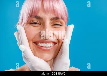 Nahaufnahme einer lächelnden Frau. Hände der Kosmetikerin, die das weibliche Gesicht untersuchen, bevor sie Botox-Injektionen verabreichen Stockfoto