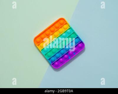 POPIT oder einfaches Spielzeug mit Grübchen, Draufsicht auf blauem Hintergrund mit zwei Schatten. POPIT auf blauem Hintergrund, Kopierbereich. Beliebte Silikon bunte Anti-Stress Pop it Kinderspielzeug. Draufsicht von oben. Einfache Grübchen Stockfoto
