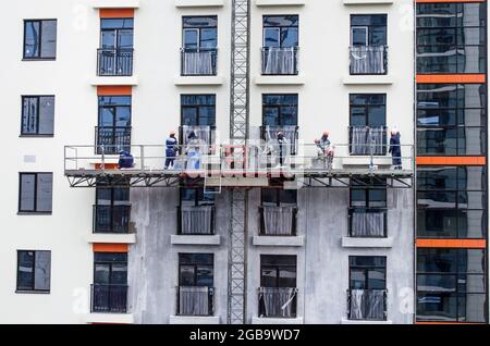 Arbeiter in gelber Hängevorrichtung montiert Umweltplatten zur Isolierung auf einem neu gebauten Hochhaus Stockfoto