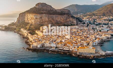 Sonnenaufgang über dem Hafen in Cefalu, Sizilien, Italien, Panorama-Luftaufnahme der Altstadt mit bunten Häusern am Wasser, Meer und La Rocca Klippe.attraktiv Stockfoto