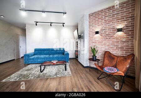 Vorderansicht des Wohnzimmers mit stilvoller moderner Einrichtung mit großem gemütlichen blauen Sofa, schöner grauer Matte und modischen Lampen. Konzept des modernen Wohnzimmers mit interessanten Farben. Stockfoto