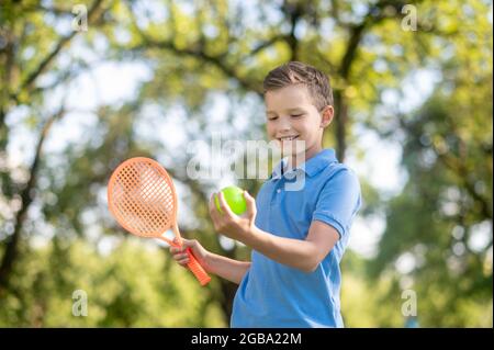 Lächelnder Junge, der den Tennisball in der Hand betrachtet Stockfoto