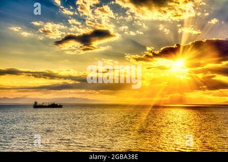 Eine Silhouette eines Frachtschiffes bei Sonnenuntergang. Ruhiges Meer mit Sonnenuntergang Himmel und Sonne durch die Wolken über. Meditation Ozean und Himmel Hintergrund. Stockfoto