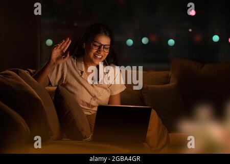 EINE JUNGE FRAU, DIE BEI VIDEOKONFERENZEN IN DER NACHT LACHT Stockfoto