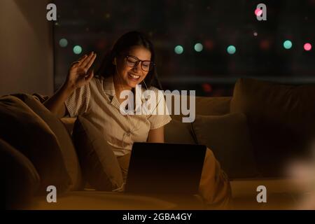 EINE JUNGE FRAU, DIE BEI VIDEOKONFERENZEN IN DER NACHT LACHT Stockfoto