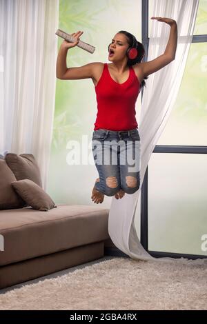 EINE JUNGE FRAU SPRINGT FRÖHLICH, WÄHREND SIE SINGT UND ZUR MUSIK TANZEND Stockfoto