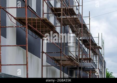 Gerüst gegen dunkelgraues Gebäude mit weißen Fenstern. Wunderschöne Fassade mit sich wiederholenden quadratischen Fenstern. Moderne Architektur. Branche. Selektiv f Stockfoto