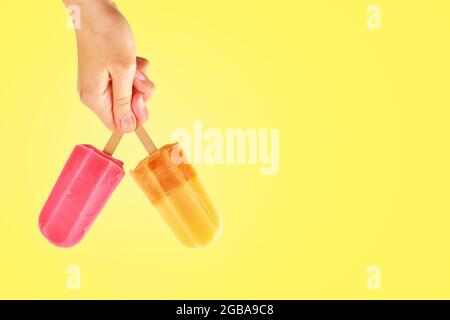 Buntes Eis in Frauenhand auf gelbem Hintergrund mit Kopierraum. Sommerhintergrund Stockfoto