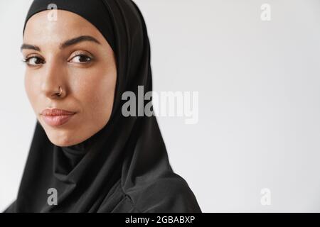 Eine Nahaufnahme der muslimischen Frau im Hijab, die im weißen Studio auf die Kamera schaut Stockfoto