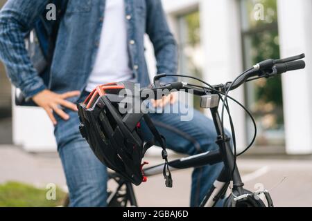 Nahaufnahme eines Fahrradhelms, der am Lenker eines Fahrrads hängt, das am Sommertag auf der Straße der Stadt auf verschwommenem Hintergrund steht Stockfoto