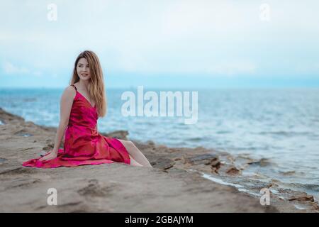 Junge Frau in einem rosa Kleid sitzt am Strand Stockfoto