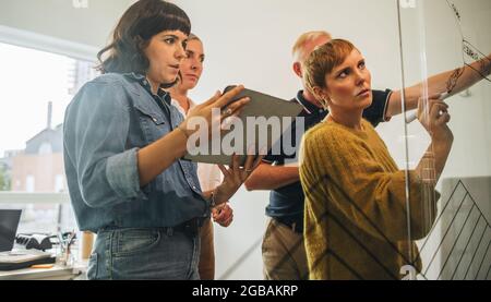 Team plant neue Geschäftsstrategie auf Glaswand. Unternehmerin schreibt an einer Glaswand und diskutiert ihre Ideen mit dem Team. Stockfoto
