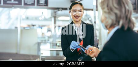 Das Sicherheitspersonal des Flughafens checkte den Passagier ein. Der Bodenwächter mit Gesichtsschutz unterstützt den Reisenden am Abflugsteig. Stockfoto