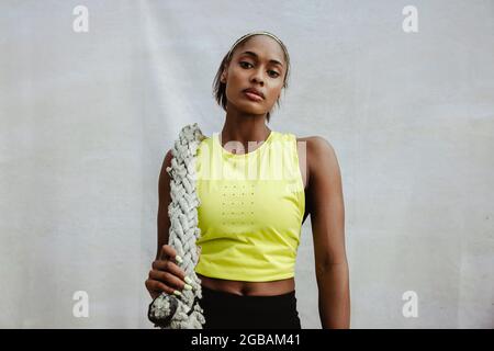 Fit Frau in Sportkleidung stehend mit Kampfseil. Selbstbewusste Sportlerin, die nach dem Training das Kampfseil hält und sich entspannt. Stockfoto