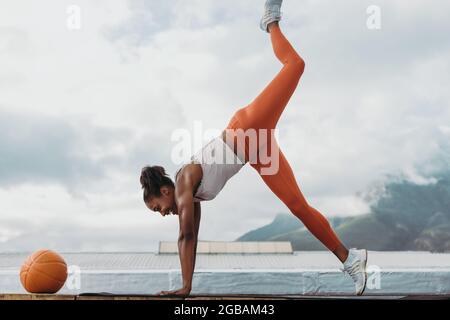 Frau in Sportkleidung mit Medizinball vor tun Stretching Yoga-Training im Freien. Die Sportlerin balanciert ihren Körper auf den Händen auf dem Dach. Stockfoto