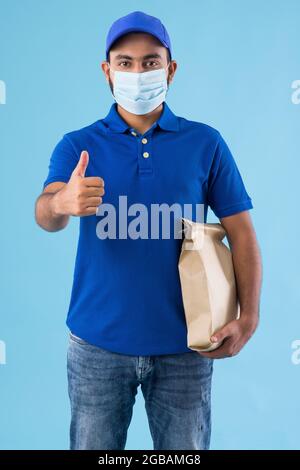 EIN LIEFERER TRÄGT EINE GESICHTSMASKE UND STEHT MIT EINER LEBENSMITTELVERPACKUNG Stockfoto