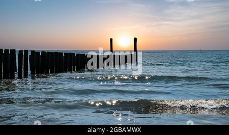 Friedlicher und romantischer Hintergrund mit Wellenbrechern am Strand bei Sonnenuntergang. Stockfoto