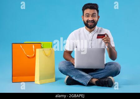 EIN BÄRTIGER JUNGER MANN, DER GERNE MIT EINER DEBITKARTE ONLINE EINKAUFEN GEHT Stockfoto