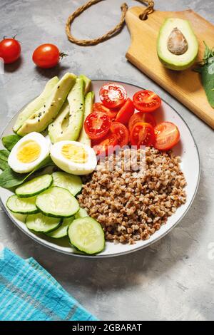 Vegane Lunchschale mit Avocado, Ei, Gurke, Tomaten und Buchweizen auf betontem Hintergrund Stockfoto