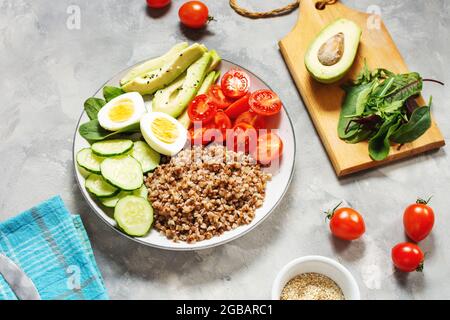 Vegane Lunchschale mit Avocado, Ei, Gurke, Tomaten und Buchweizen auf betontem Hintergrund Stockfoto