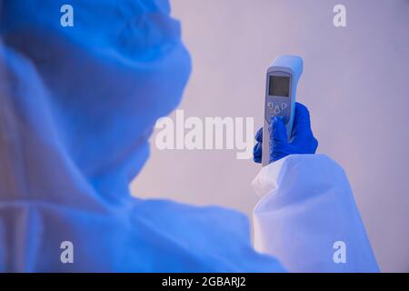 Ein Mitarbeiter im Gesundheitsbereich, der eine Temperaturkontrollpistole in einem PSA-Kit hält. Stockfoto