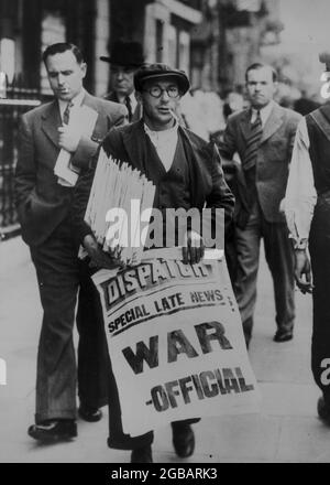 LONDON, ENGLAND, Großbritannien - 3-4. September 1939 - EIN Zeitungsverkäufer, der Stapel von Zeitungen hält und in Whi ein Schild mit der Aufschrift „Special Late News: War - Official“ ausstellt Stockfoto