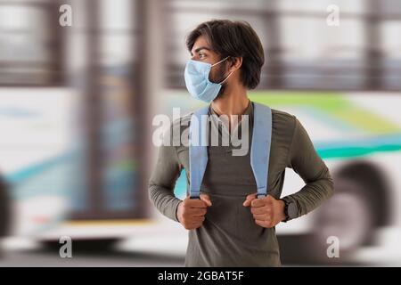 Eine junge Studentin mit Gesichtsmaske, die vor einem Bus steht. Stockfoto