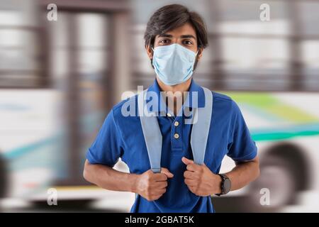 Eine junge Studentin mit Gesichtsmaske, die vor einem Bus steht. Stockfoto