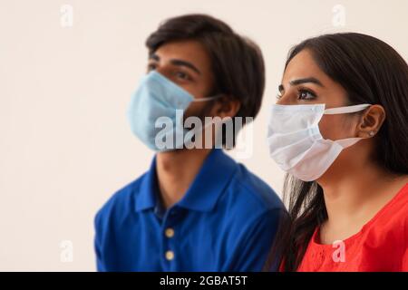 Ein junger Mann und eine junge Frau sitzen zusammen mit Masken auf ihrem Gesicht. Stockfoto