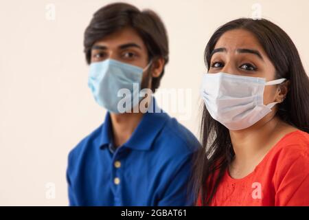 Ein junger Mann und eine junge Frau sitzen zusammen mit Masken auf ihrem Gesicht. Stockfoto