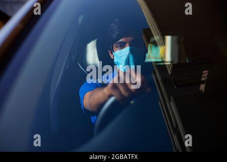 Ein junger Mann, der mit Gesichtsmaske in seinem Auto sitzt. Stockfoto