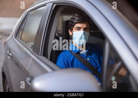 Ein junger Mann, der mit Gesichtsmaske in seinem Auto sitzt. Stockfoto