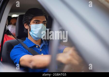 Ein junger Mann mit Gesichtsmaske, der sein Auto fährt. Stockfoto