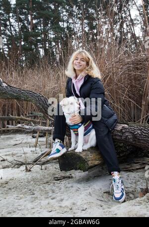 Teenager schönes Mädchen geht mit ihrem Lieblingstier, weißen Hund, im kalten Winter oder Herbst im Freien. Aktiver Lebensstil, digitale Entgiftung, Lebensfreude Stockfoto