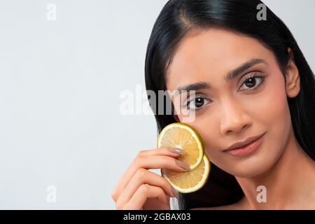 Eine junge Frau mit klarer, makelloser Haut, die zwei Zitronenscheiben hält. Stockfoto