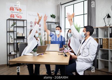 Wissenschaftlicher Durchbruch. Eine Gruppe von vier verschiedenen medizinischen Spezialisten, die nach langen und harten Diskussionen im Büro Papiere aufwarfen. Mit Erfolg zu einem Treffen überkommen. Internationale Zusammenarbeit. Stockfoto