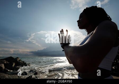 Schön für junge Sportlerin, die bei der Meditation in den Strahlen der untergehenden Sonne Namaste-Mudra macht Stockfoto