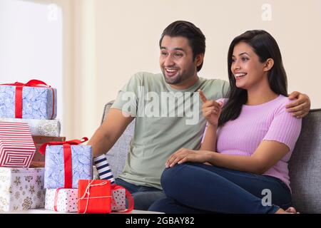 Ein junger Mann und eine junge Frau sitzen glücklich im Zimmer mit Geschenkboxen daneben. Stockfoto