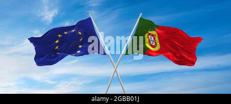 Flaggen der Europäischen Union und portugals winken im Wind auf Fahnenmasten gegen den Himmel mit Wolken am sonnigen Tag. Symbolisieren Beziehung, Dialog zwischen t Stockfoto