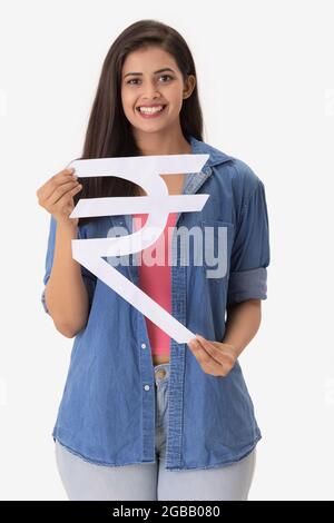 Eine junge Frau, die das indische Rupie-Symbol aus Pappe in der Hand hält. Stockfoto