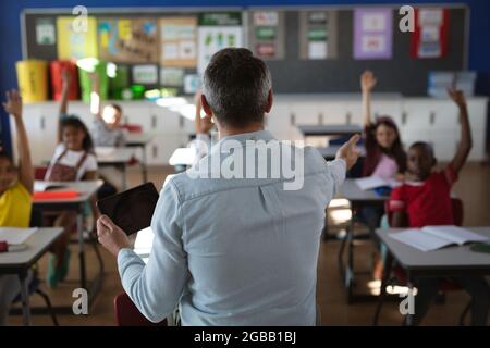 Rückansicht des kaukasischen männlichen Lehrers, der während des Unterrichts in der Schule ein digitales Tablet verwendet Stockfoto