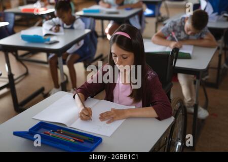 Kaukasisches Mädchen, das in der Schule auf ihrem Schreibtisch sitzt Stockfoto