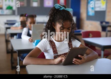 afroamerikanisches Mädchen mit digitalem Tablet, während es in der Schule auf ihrem Schreibtisch sitzt Stockfoto