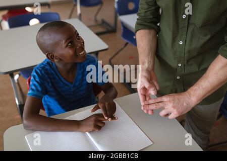 Mittlerer Abschnitt des männlichen Lehrers, der in der Hand Gebärdensprache mit afroamerikanischem Jungen in der Schule spricht Stockfoto